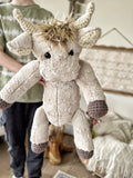 Person holding a handmade highland cow plush toy in a cozy indoor setting