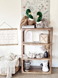 Wooden shelf with decorative items including stuffed animals and a basket in a room setting.