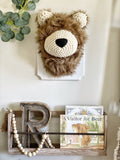 A plush Brown Bear Wall Mount handmade by ClaraLoo with soft faux fur and crocheted accents. This stuffed bear is mounted on a white wooden plaque and is hung on the wall of a woodland themed nursery.