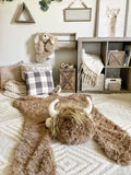 A plush highland cow rug made by ClaraLoo on the floor of a farm themed nursery. The highland cow features brown faux fur and crocheted accents.