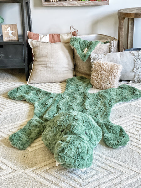 A green plush T-Rex rug on the floor of a dinosaur themed nursery.