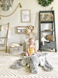 A small child sitting on a plush gray elephant rug on the floor of a safari themed bedroom.