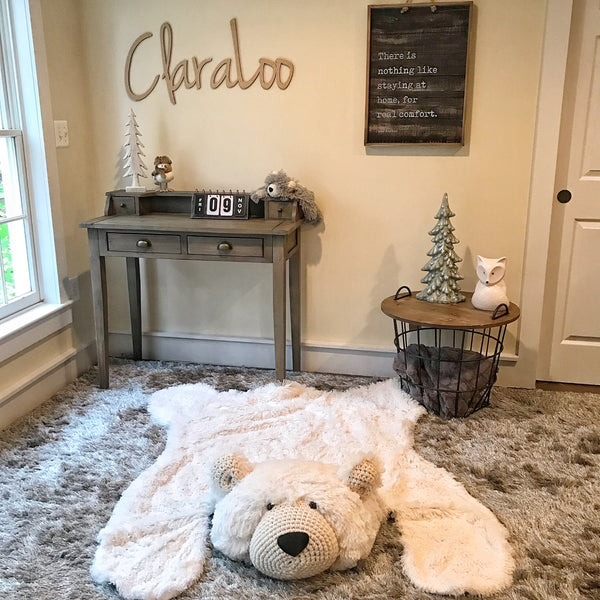 A large white polar bear rug made with plush faux fur and crocheted accents. The bear rug is on top of a shaggy gray carpet.