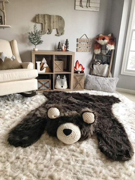 A large brown bear rug on a cream colored carpet in a woodland themed bedroom. The bear rug is made by ClaraLoo with plush faux fur. The animal rug has cream colored ears and face with a black nose.
