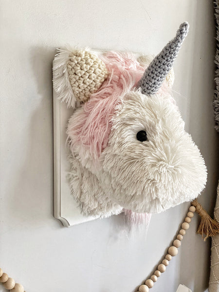 A plush Unicorn Wall Mount handmade by ClaraLoo in a fantasy themed nursery. This stuffed unicorn is made of white faux fur with crocheted ears and a crocheted horn. This plush unicorn is mounted on a white wooden plaque.